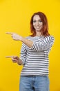 Happy excited cuacaisan winsome ginger girl in striped shirt pointing with two fingers isolated on golden yellow background