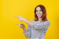 Happy excited cuacaisan winsome ginger girl in striped shirt pointing with two fingers isolated on golden yellow background