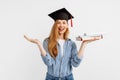 Happy excited beautiful girl graduate with a graduation hat on her head, holding books and having fun standing on a white Royalty Free Stock Photo