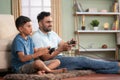 Happy excited indian father with son playing video game using joystick on floor at home - concept of Joyful playtime Royalty Free Stock Photo
