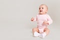 Happy excited infant child baby girl toddler wearing bodysuit and socks sitting on floor isolated on white background looking away Royalty Free Stock Photo
