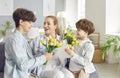 Happy excited mother getting spring flowers from grateful grown teen and small son at home