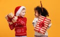 Happy excited multiracial children in Christmas outfit holding Xmas gifts against yellow background