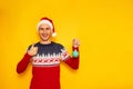 happy excited smiling man in Christmas sweater with reindeer, red Santa Claus hat holds Christmas tree toy in his hands Royalty Free Stock Photo