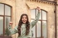 Happy excited teenage girl shouting making winner gesture in casual style blurry outdoors