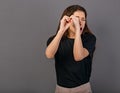 Happy excited woman doing spyglass sign looking in by fingers the hands with surprising opened mouth in black t-shirt. Concept Royalty Free Stock Photo