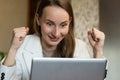 A happy, excited young female office worker raises her hands and screams with joy, celebrating a successful online Royalty Free Stock Photo