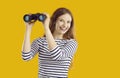 Happy, excited young woman looking through binoculars isolated on yellow background Royalty Free Stock Photo