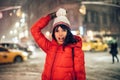 Happy exited woman having fun on city street of New York under the snow at winter time wearing hat and jacket.