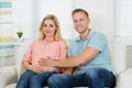 Happy Expectant Couple Sitting On Sofa At Home