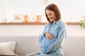 Happy expectant pregnant young woman sits on living room sofa Royalty Free Stock Photo