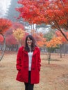 Happy eyeglasses Asian woman in red coat standing in cold colorful autumn trees garden park