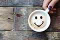 Happy face on cappuccino foam, woman hands holding one cappuccino cup on wooden table Royalty Free Stock Photo