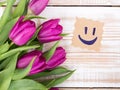 Happy face on paper and bouquet of tulips on wooden background