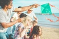 Happy families flying with kite and having fun on the beach - Multi ethnic couples playing with children on weekend vacation - Royalty Free Stock Photo