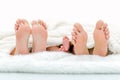 Happy familiy in bed. Mother father and baby feet under blanket. Tree pairs of legs. Royalty Free Stock Photo