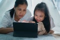 Happy family of Asian mother and daughter using tablet in a tent at night. Asia children hug a doll, talk, and learning on the Royalty Free Stock Photo
