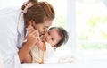 Happy family. Asian mother kissing her adorable Caucasian newborn 3 months old baby girl cheek, having fun playing together while Royalty Free Stock Photo