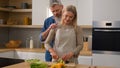 Happy family Caucasian middle-aged adult at kitchen woman cook vegetable salad cut cucumber husband man hugging cuddling Royalty Free Stock Photo