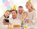 A happy family celebrating a birthday with a party, wearing hats and taking a selfie using a phone. Mature man taking a Royalty Free Stock Photo