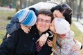 Happy family of 4 celebrating: Parents with two children having fun hugging & kissing father who is happy smile, closeup portrait