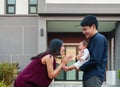 happy family, cheerful father and mother holding and playing with newborn baby while standing in front of their house