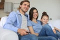 Happy family with child sitting on sofa watching tv, young parents embracing daughter relaxing on couch together Royalty Free Stock Photo