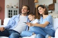 Happy family with child sitting on sofa watching tv, young parents embracing daughter relaxing on couch together Royalty Free Stock Photo