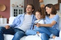 Happy family with child sitting on sofa watching tv, young parents embracing daughter relaxing on couch together Royalty Free Stock Photo