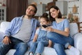 Happy family with child sitting on sofa watching tv, young parents embracing daughter relaxing on couch together Royalty Free Stock Photo