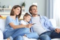 Happy family with child sitting on sofa watching tv, young parents embracing daughter relaxing on couch together Royalty Free Stock Photo