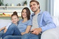 Happy family with child sitting on sofa watching tv, young parents embracing daughter relaxing on couch together. Royalty Free Stock Photo