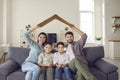 Happy family with children sitting at home on the couch under a symbolic cardboard roof. Royalty Free Stock Photo
