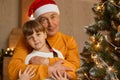 Happy family on Christmas Eve, little charming little girl with pigtails posing with her grandfather, senior man in santa claus