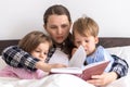 happy family. Close up loving mother lying with daughter son two kids pajamas in bed children reading interesting Royalty Free Stock Photo