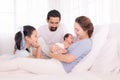 Happy family concept, father and daughter sit on bed excited looking new member in family, adorable newborn sleep on mother chest Royalty Free Stock Photo