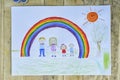 Happy family concept. Sheet with a pattern on a wooden table: parents and children hold hands against background of rainbow and