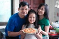 The happy family consisted of father, mother and daughter holding homemade pizza pans in the home kitchen