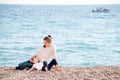 Happy dreaming family consisting of mother and little child resting on sea beach with boat on horizon in early summer day Royalty Free Stock Photo