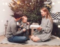 Happy family couple give gifts in the living room, behind the decorated xmas tree, the light give a cozy atmosphere. New Year