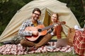 Happy family couple sitting near tent at campsite and learning to play guitar with online lesson Royalty Free Stock Photo