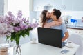 Happy family couple using laptop having coffee in kitchen during coronavirus quarantine. Young man and woman kissing Royalty Free Stock Photo