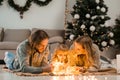 Happy family with daughter lies on the floor and cozy talks by the light of garlands against the background of Christmas tree.