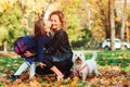 Happy family with dog on walk in autumn city park. Mother and child daughter playing with autumn leaves Royalty Free Stock Photo