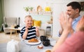 Happy family with down syndrome son at the table, clapping when having breakfast. Royalty Free Stock Photo