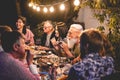 Happy family eating and drinking wine at barbecue dinner outdoor - Multiracial mature and young people having fun at bbq sunday