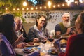 Happy family eating and drinking wine at barbecue dinner outdoor - Multiracial mature and young people having fun at bbq sunday