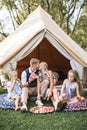 Happy family eating watermelon at picnic in meadow near the wigwam tipi tent. Mother and father kissing, and two Royalty Free Stock Photo