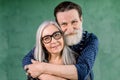 Happy family, elderly couple in love, standing on green background. Attractive smiling gray haired lady in eyeglasses