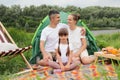 Happy family enjoying resting near the river in nature park, People sitting on ground near the tent. Weekend in open air near the Royalty Free Stock Photo